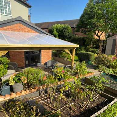 Garden with raised beds, plants, and a wooden gazebo on a sunny day.