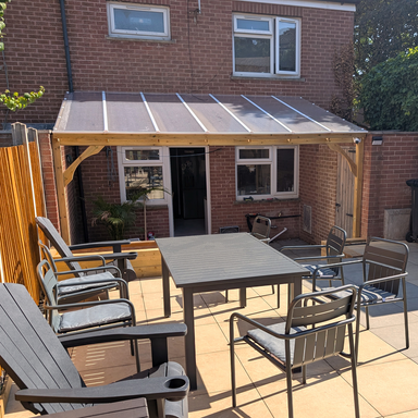 Outdoor patio area with a wooden gazebo, table, and chairs in front of a brick house.