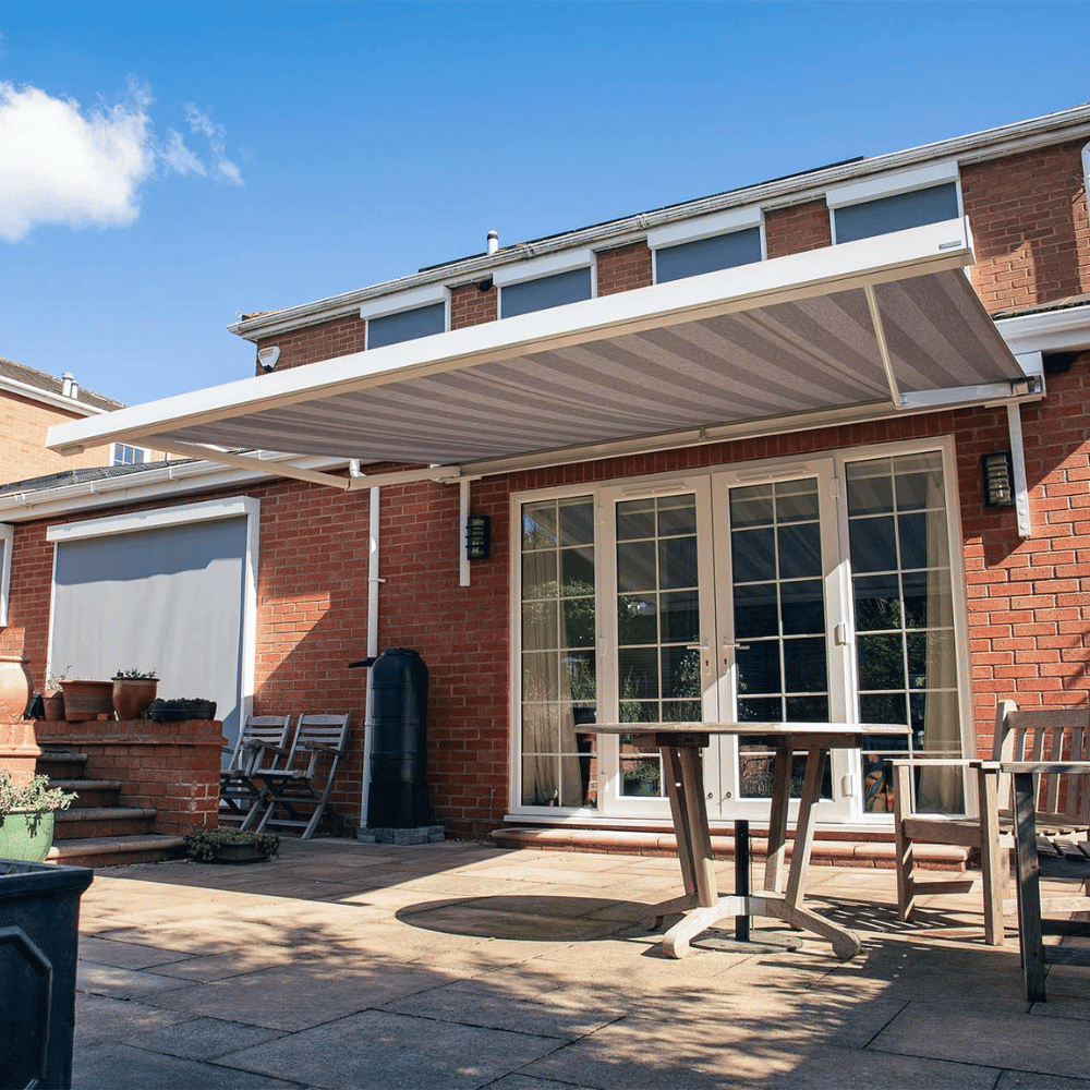 Outdoor patio with a retractable awning, table, chairs, and plants on a sunny day.