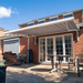Outdoor patio with a retractable awning, table, chairs, and plants on a sunny day.