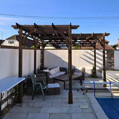Outdoor patio area with wooden pergola, furniture, and pool in the background.