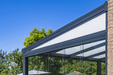 Modern glass patio cover with metal frame against a blue sky