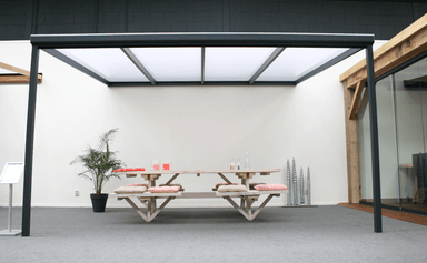 Modern outdoor dining table with benches under a metal canopy in an indoor setting.