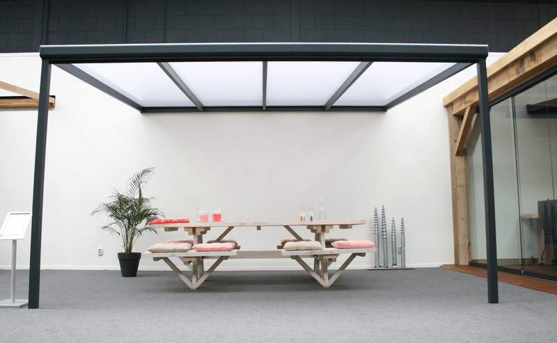 Modern outdoor dining table with benches under a metal canopy in an indoor setting.