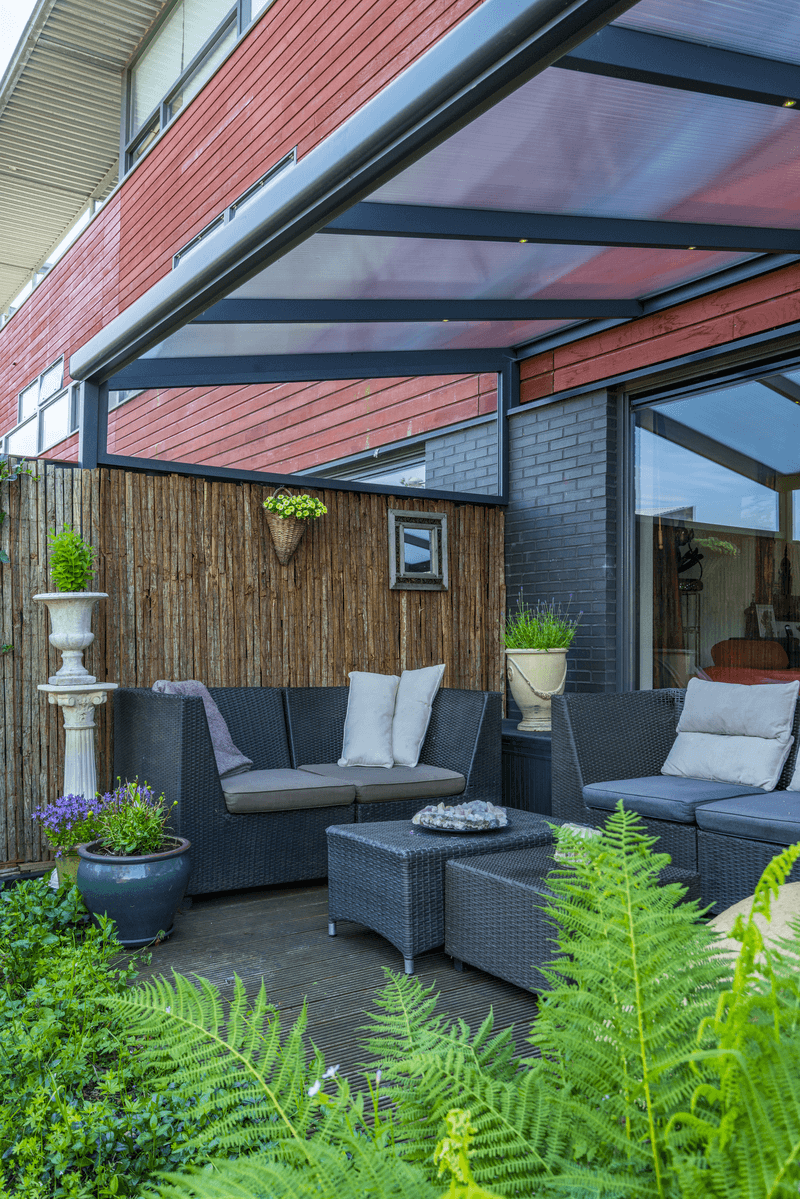 Outdoor patio with gray sectional sofa, plants, and a wooden wall.