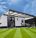 Patio cover with white roof and black frame in a garden setting with a clear blue sky.