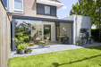 Modern house exterior with a patio area, garden, and outdoor furniture.