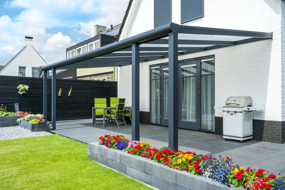 Outdoor patio with pergola, chairs, and a grill in a residential setting.