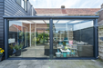 Modern glass extension connecting a house to an outdoor patio area with furniture.