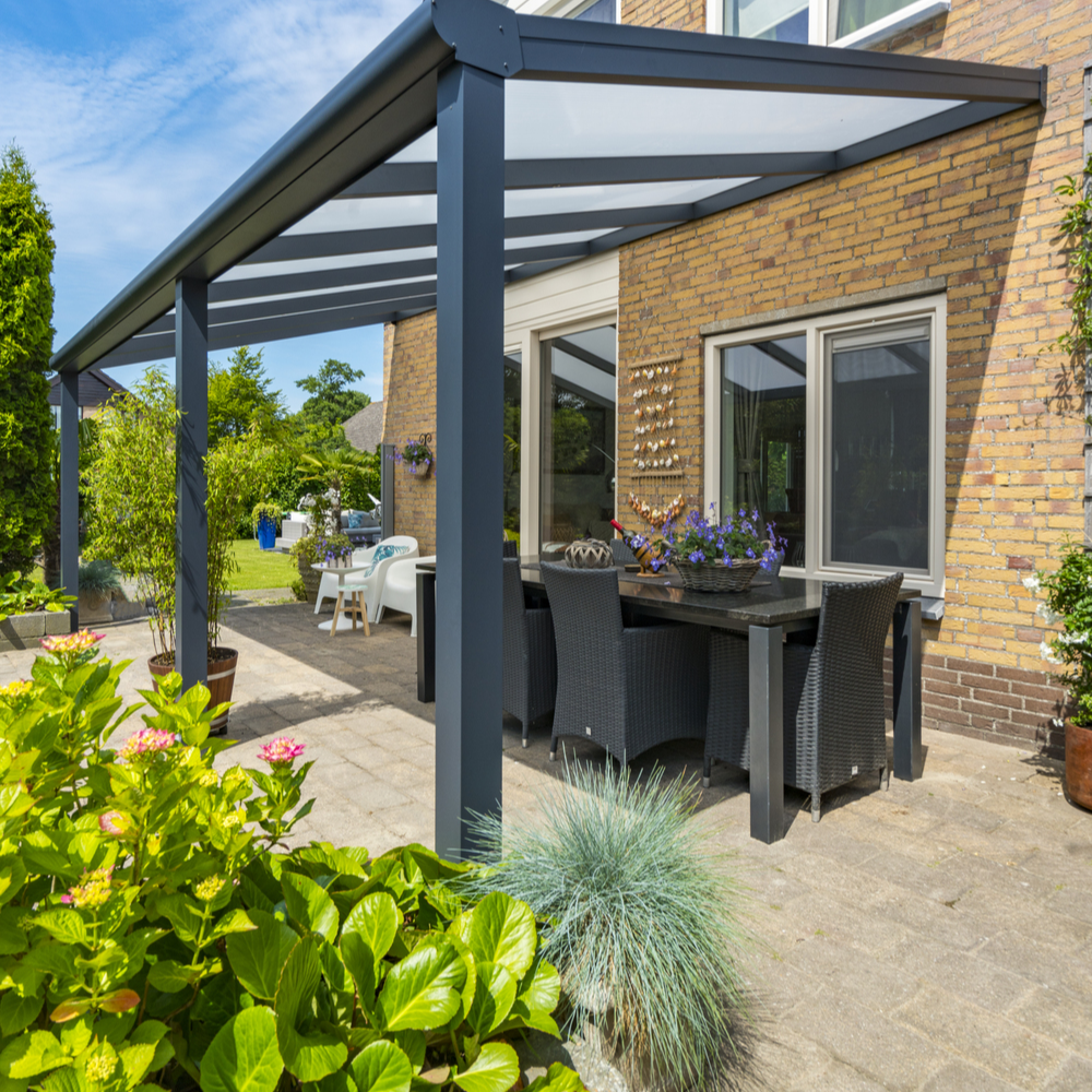 Outdoor patio area with a pergola, table, chairs, and plants on a sunny day.