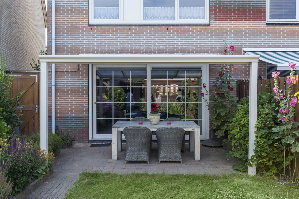 Outdoor patio area with a table and chairs under a white pergola, surrounded by a garden.
