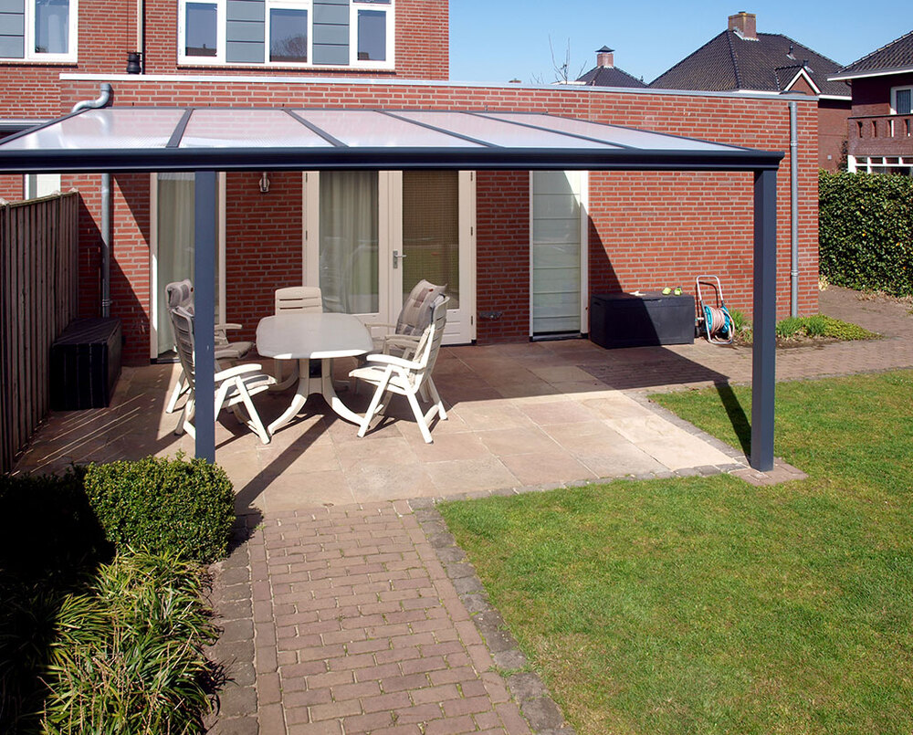 Patio area with pergola, table, and chairs in front of a brick house.