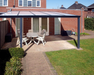 Patio area with pergola, table, and chairs in front of a brick house.