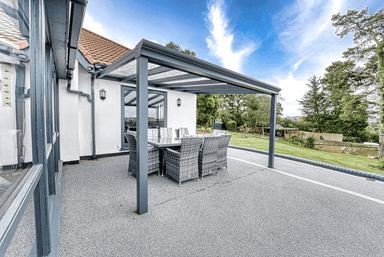 Outdoor patio area with a pergola and furniture on a driveway.
