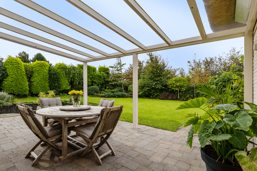 Outdoor patio with wooden table and chairs under a Deponti Pigato , surrounded by greenery.