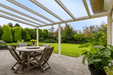 Outdoor patio with wooden table and chairs under a Deponti Pigato , surrounded by greenery.