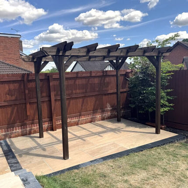 Wooden pergola on a patio area with a wooden fence and house in the background.