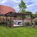 Garden with wooden pergola, outdoor furniture, and greenery under a blue sky.