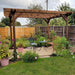 Garden with wooden pergola, chairs, and table surrounded by plants and flowers.