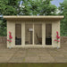 Wooden garden office with glass doors and windows, surrounded by greenery.