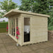 Wooden garden office with a computer setup, surrounded by greenery.