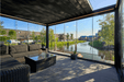 Modern outdoor patio with glass walls overlooking a canal and buildings.