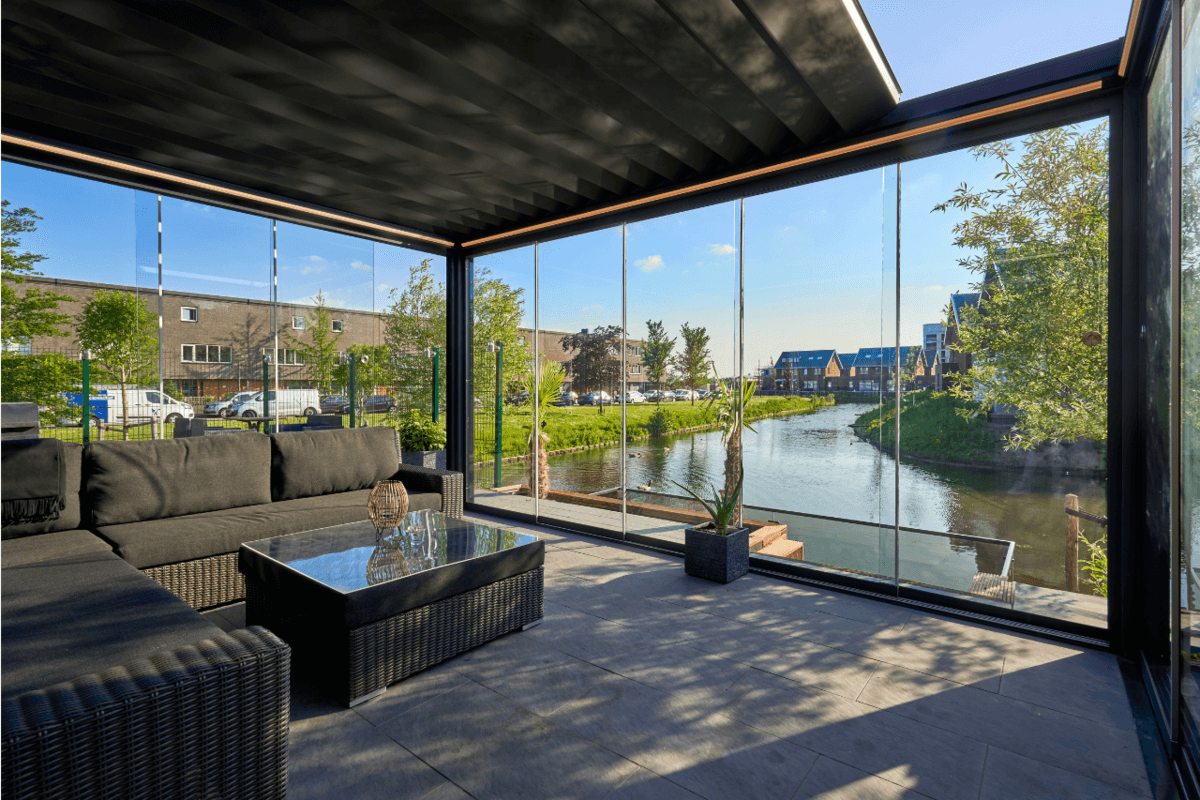 Modern outdoor patio with glass walls overlooking a canal and buildings.