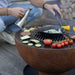 Vegetables and meat cooking on the HEAT Gystad griddle with tongs