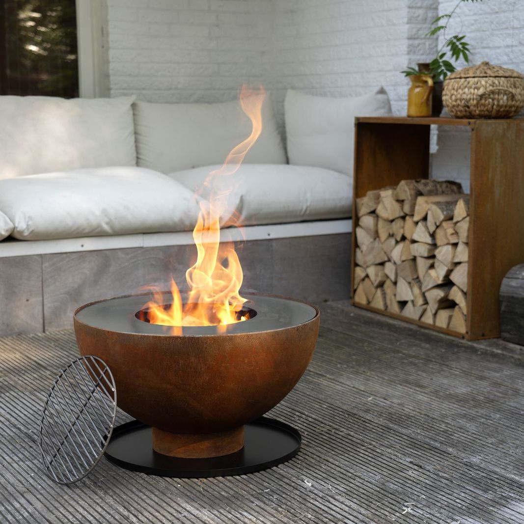 HEAT Gystad fire bowl burning on a patio by a sofa and log store