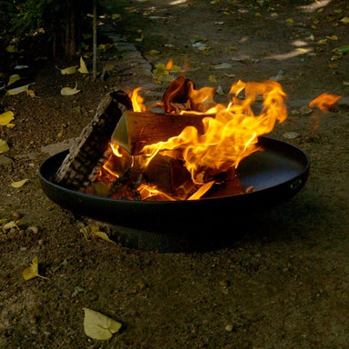 HEAT Classic black fire bowl with a roaring log fire in a woodland garden
