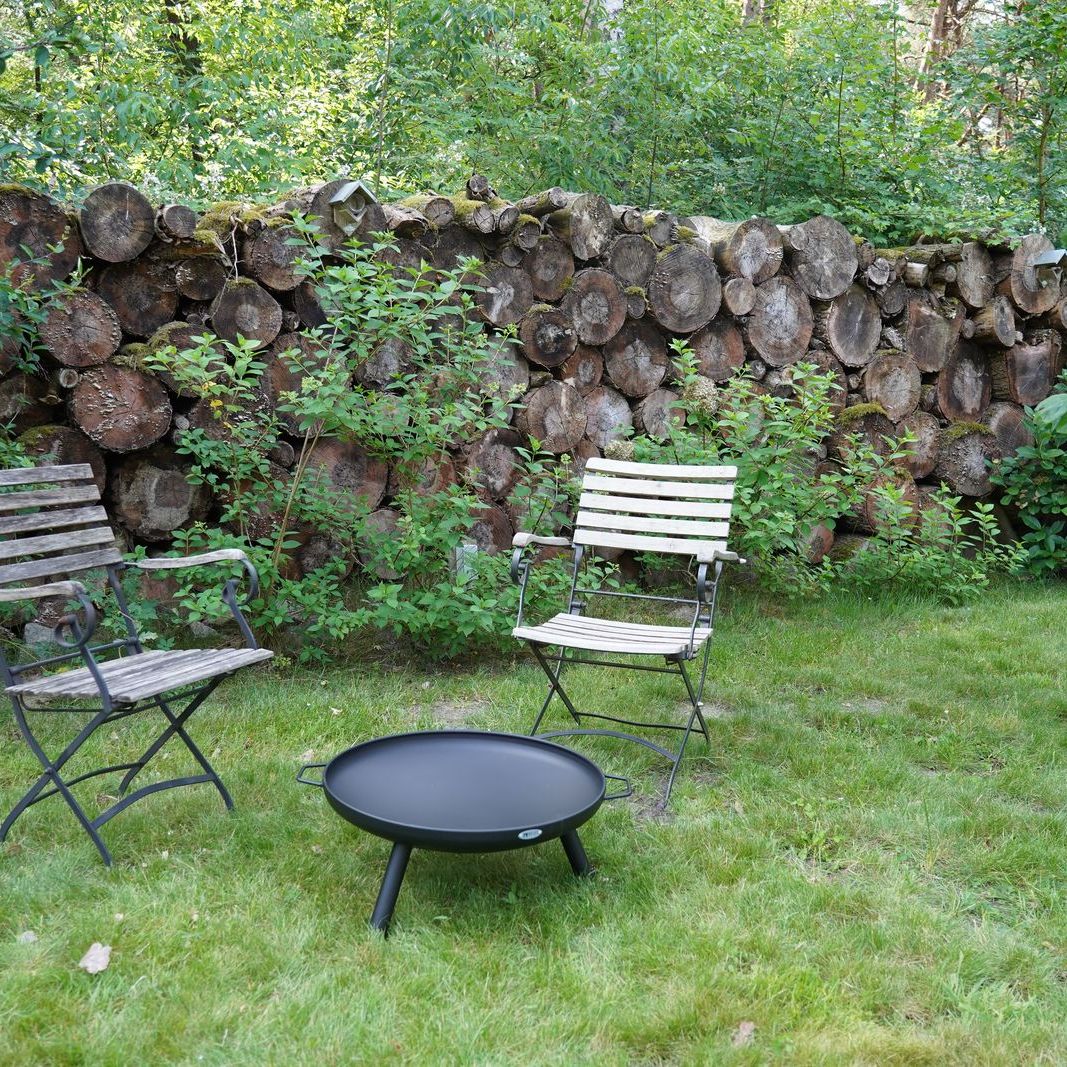 HEAT Classic black fire bowl on legs on a garden lawn with two folding chairs