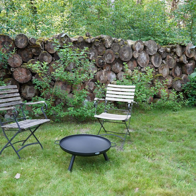 HEAT Classic black fire bowl on legs on a garden lawn with two folding chairs
