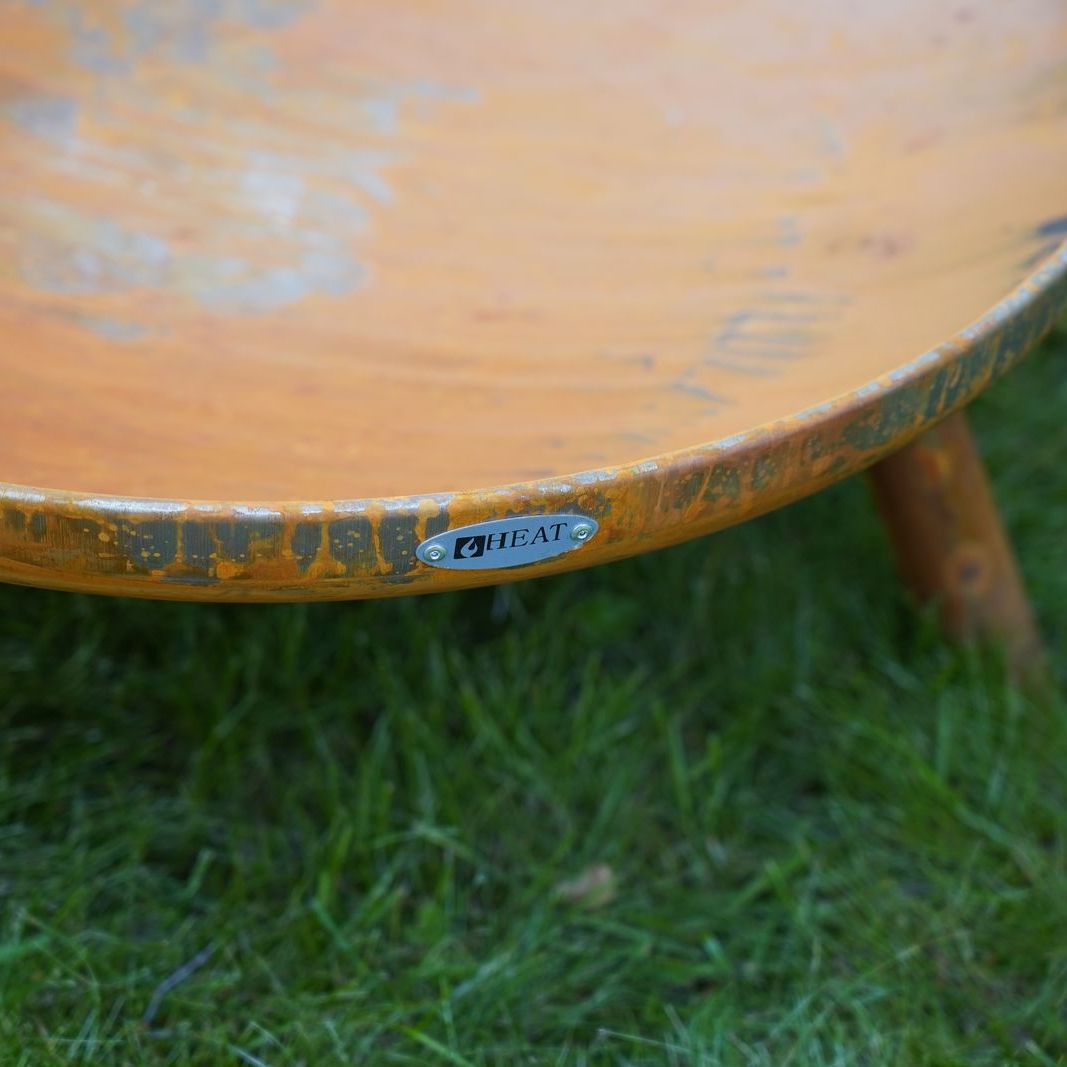 Close-up of a HEAT Classic rust fire bowl rim and wooden-look leg on grass