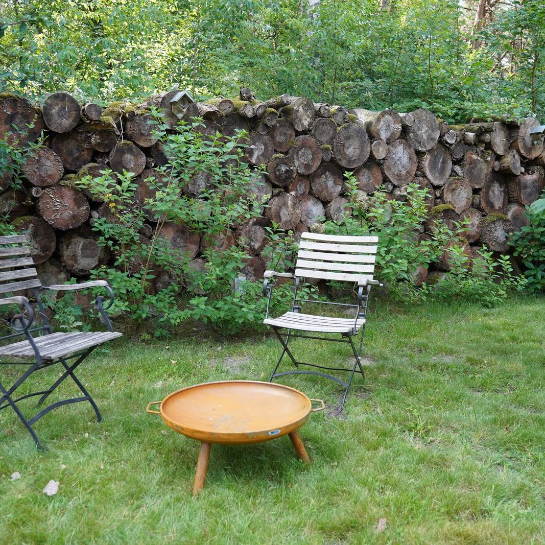 HEAT Classic rust fire bowl on legs on a lawn with garden chairs and log wall