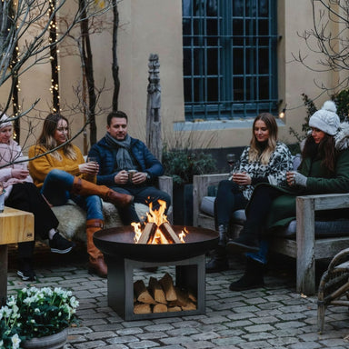 Friends round a HEAT Fresvik fire bowl on a courtyard patio