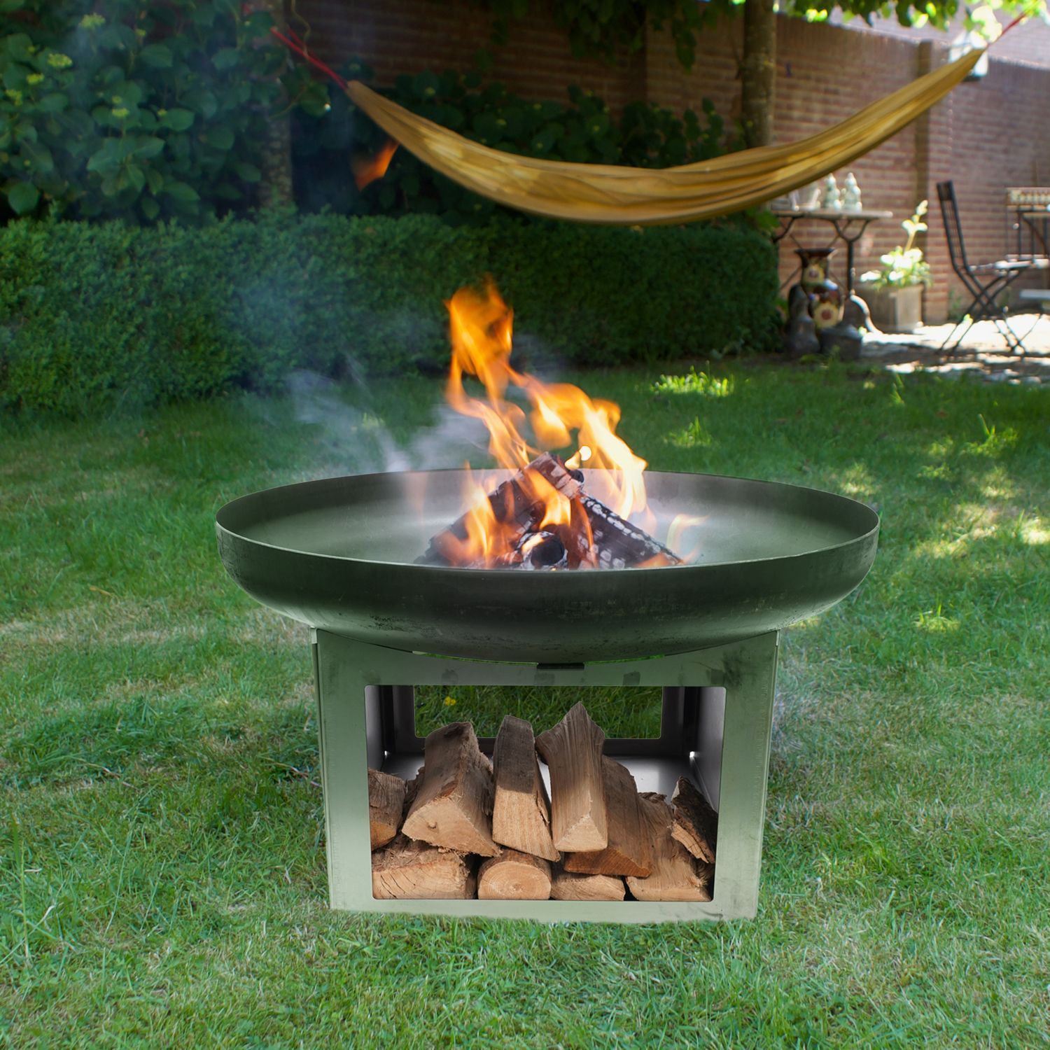HEAT Fresvik fire bowl burning on a garden lawn with logs below
