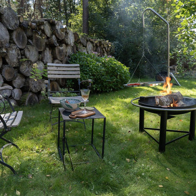 HEAT Pendal fire bowl and grill on a garden lawn with chairs and a log wall