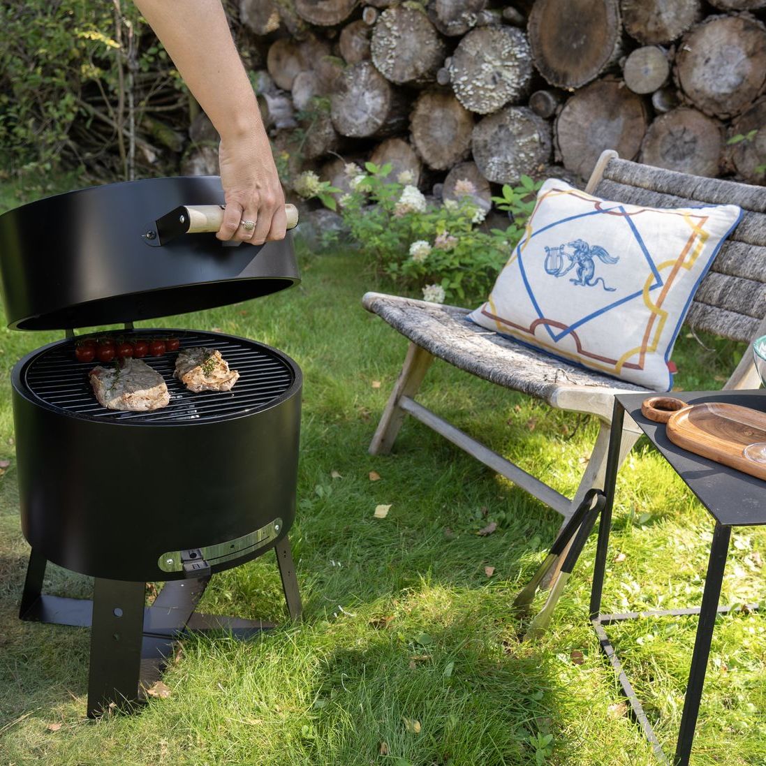 Lifting the lid of the HEAT Braten BBQ on a garden lawn