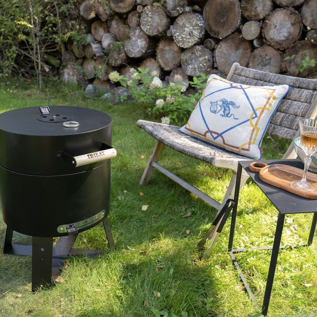 HEAT Braten compact charcoal BBQ with lid closed beside a garden chair