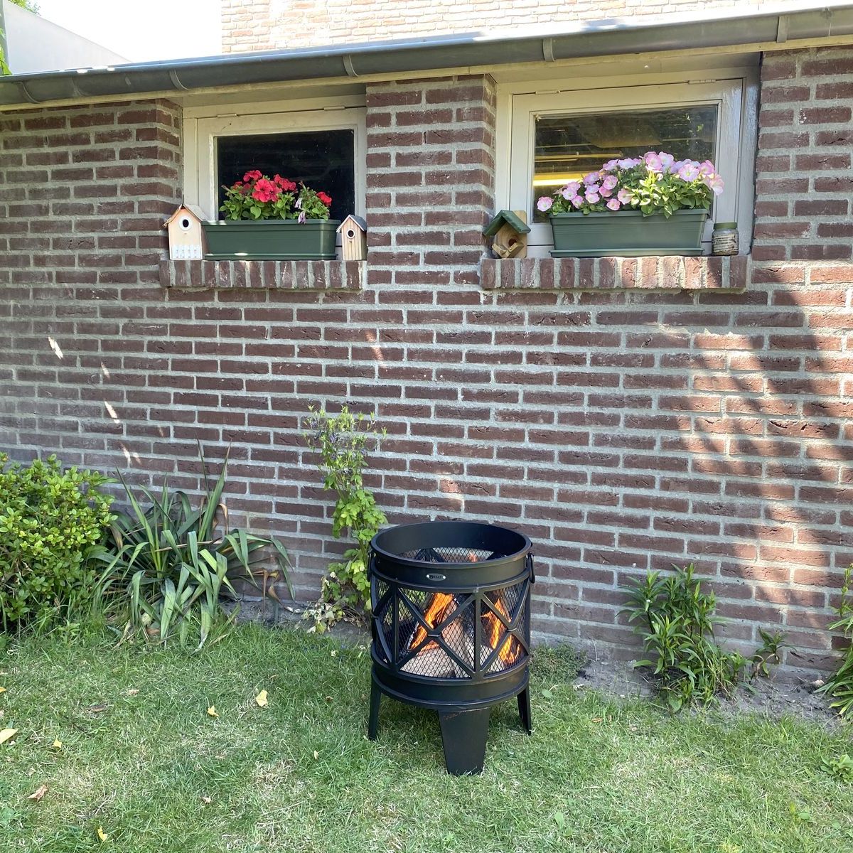HEAT FireCask with a fire glowing, on a lawn by a brick wall