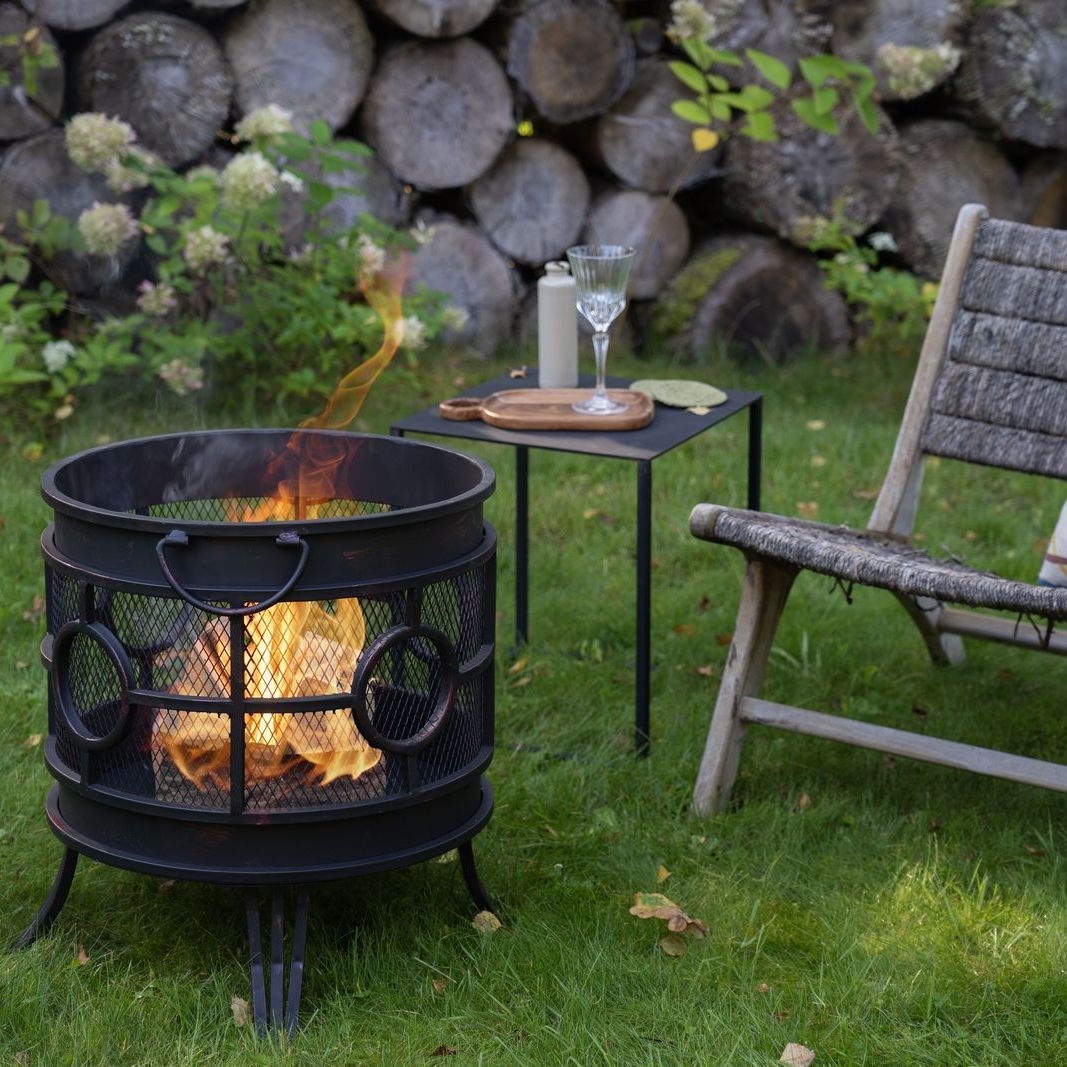 HEAT Tynset fire basket burning on a lawn beside a garden chair and side table