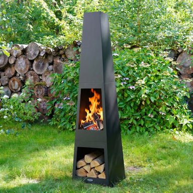HEAT Oslo outdoor fireplace lit with logs stored below, in a garden