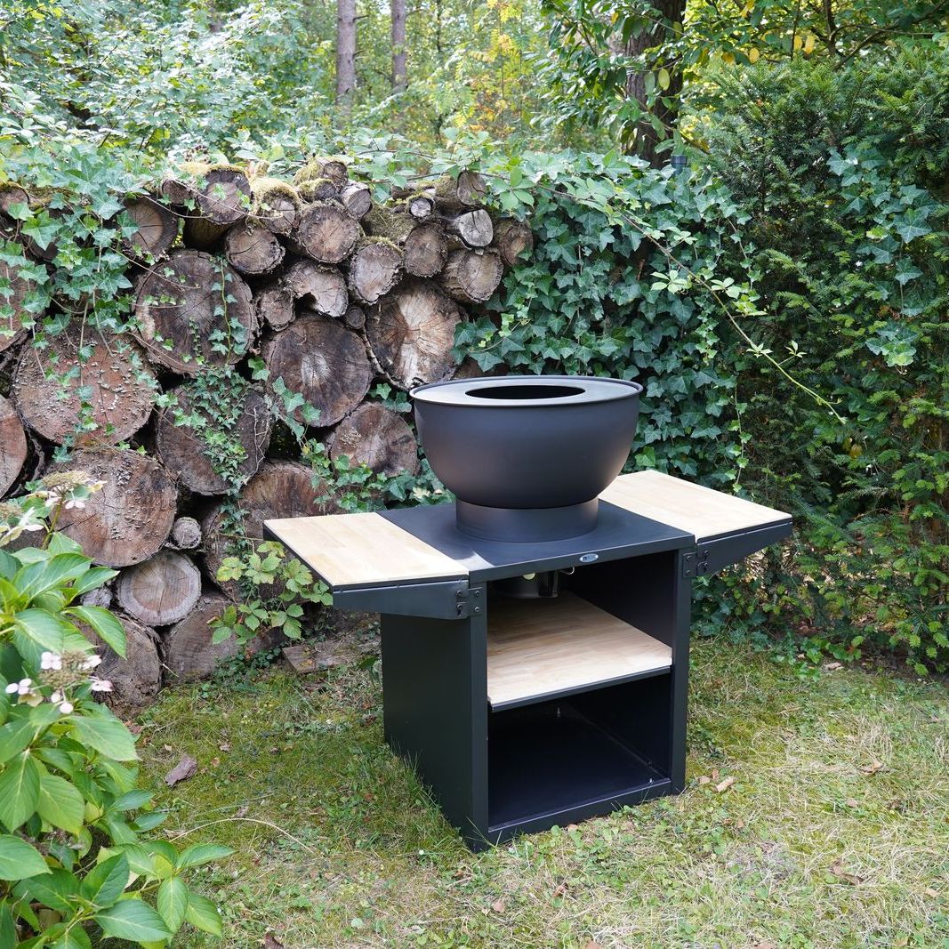 HEAT Kjok black outdoor kitchen with fire bowl in front of a log wall