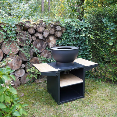 HEAT Kjok black outdoor kitchen with fire bowl in front of a log wall