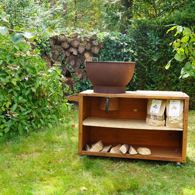 HEAT Trolle rust outdoor kitchen unit on a lawn with bags of fuel on the shelf