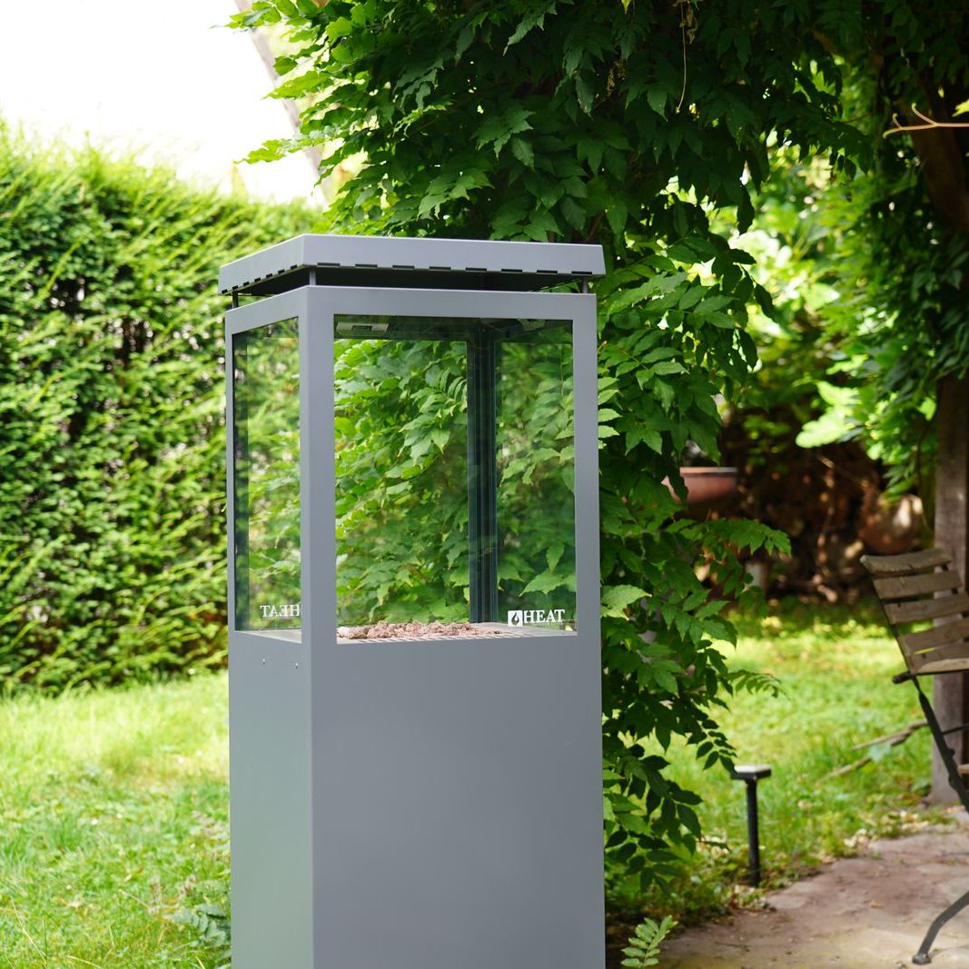 HEAT Utevarme patio heater beside a garden table and hedge