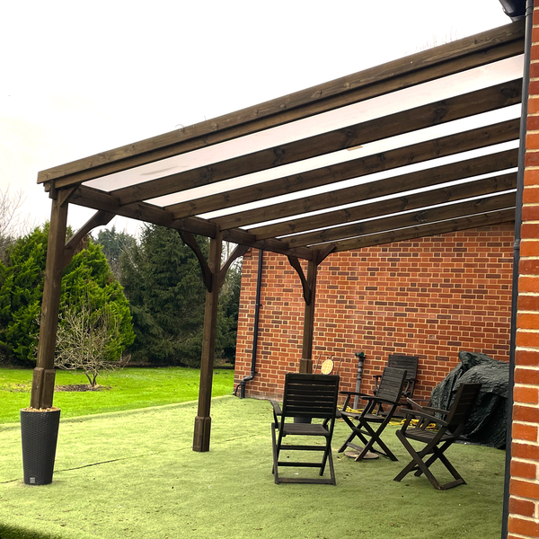 Wooden gazebo with outdoor furniture on a grassy area next to a brick wall.